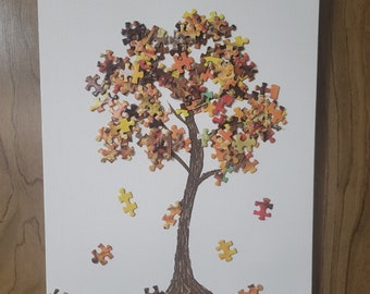 May include: A white canvas with a brown tree drawn on it. The tree is made of colorful puzzle pieces in shades of orange, yellow, brown, and red. The puzzle pieces are falling off the tree.