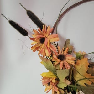 May include: A fall-themed wreath with orange and yellow flowers, brown twigs, and green leaves.