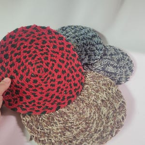 May include: Four round woven trivets in different patterns. One trivet is red with black polka dots, one is brown and white, one is gray and white, and one is blue and white.