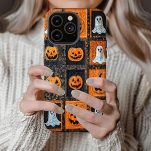 May include: A black phone case with a Halloween theme. The case features a patchwork design with orange pumpkins, white ghosts, and black and white patterns.