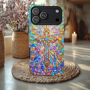 May include: A colorful phone case with a stained glass design featuring a gold cross. The case has a vibrant mix of blues, purples, oranges, and greens. The phone case is on a woven mat.