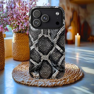 Op de afbeelding: Een smartphonehoesje met een gedetailleerd slangenleerpatroon in zwart, grijs en wit. Het hoesje heeft een opvallende camera-uitsparing linksboven, die drie ronde lenzen en een flitser voor een modern mobiel apparaat laat zien.