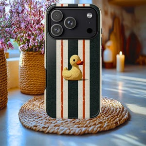May include: A black smartphone case featuring a vertical striped pattern in black, white, and thin orange lines. Centered on the back is a yellow rubber duck graphic with an orange beak. The case has a cutout for a triple-lens camera system.