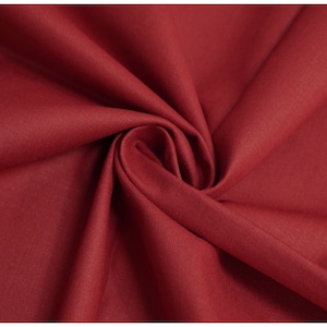 May include: Close-up of a deep red fabric with a smooth, even texture. The fabric is folded and draped, showcasing its soft, flowing quality.