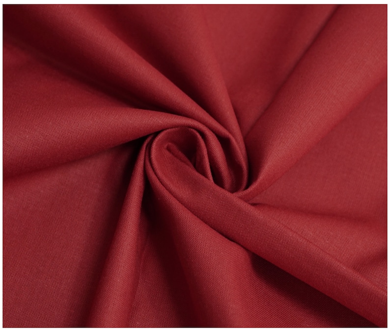 May include: Close-up of a deep red fabric with a smooth, even texture. The fabric is folded and draped, showcasing its soft, flowing quality.