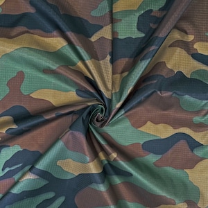 May include: Camouflage fabric in shades of green, brown, and tan. The material has a subtle sheen and a textured appearance. The pattern is a classic military-style design, suitable for various crafting and apparel projects.