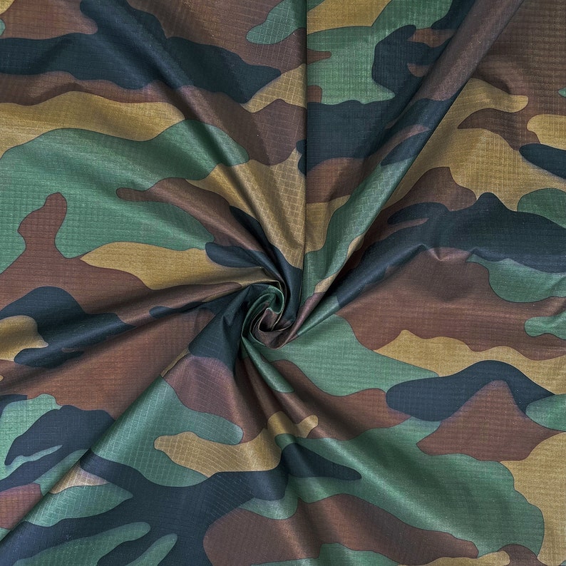 May include: Camouflage fabric in shades of green, brown, and tan. The material has a subtle sheen and a textured appearance. The pattern is a classic military-style design, suitable for various crafting and apparel projects.