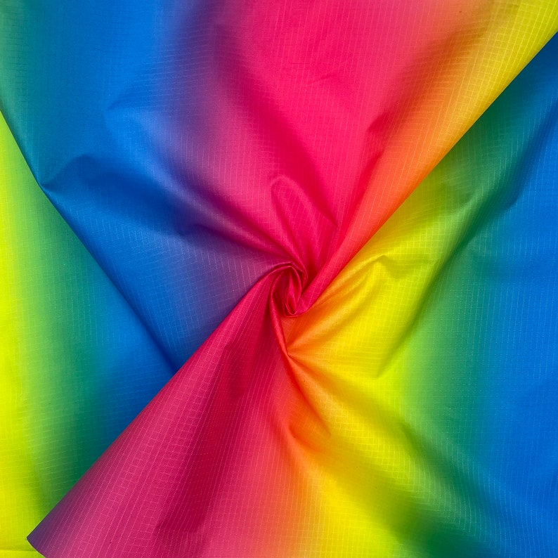 May include: A vibrant rainbow-colored fabric with a subtle grid pattern. The colors transition smoothly from red to orange, yellow, green, blue, and purple. The fabric is gathered in a spiral, creating a dynamic visual effect.
