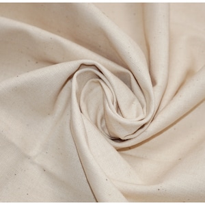 May include: Close-up of a natural off-white fabric with a slightly textured surface. The fabric is folded and draped, showcasing its soft and drapey quality.