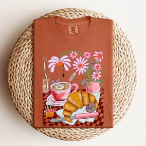 Koszulka Comfort Color z francuskim croissantem i kawą, rysowana ręcznie w stylu kreskówkowym scena kontynentalnego śniadania z uroczymi myszami, prezent dla miłośnika gryzoni.