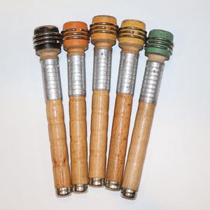 May include: Five cylindrical wooden tools with light brown handles, silver-colored metal midsections, and colored tops in black, orange, tan, yellow, and green. Each top features three horizontal metal rings encircling the colored wooden end piece.