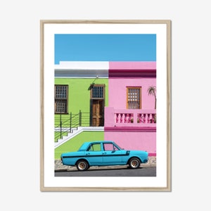 Peut inclure: Une voiture bleue vintage garée devant des maisons colorées peintes en vert, rose et blanc. Les maisons ont des bordures et des fenêtres blanches. La voiture a une bande noire sur le côté et une plaque d'immatriculation noire.