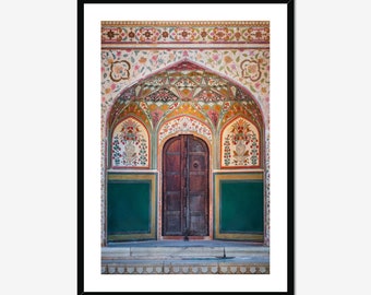 May include: A colorful, ornate doorway with a wooden door and intricate floral designs. The doorway is framed by a green archway and a white wall with floral patterns.