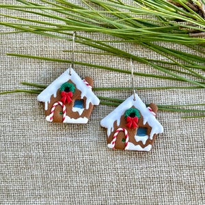 May include: A pair of gingerbread house earrings with white icing, red candy canes, and a green wreath with a red bow.