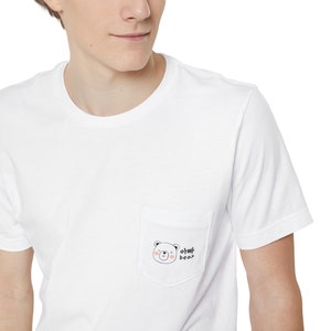 May include: White t-shirt with a pocket featuring a cartoon bear with the text "oh my bear" in black and pink.