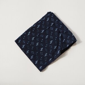 Può includere: Un pezzo di stoffa blu indaco piegato con un motivo geometrico bianco.
