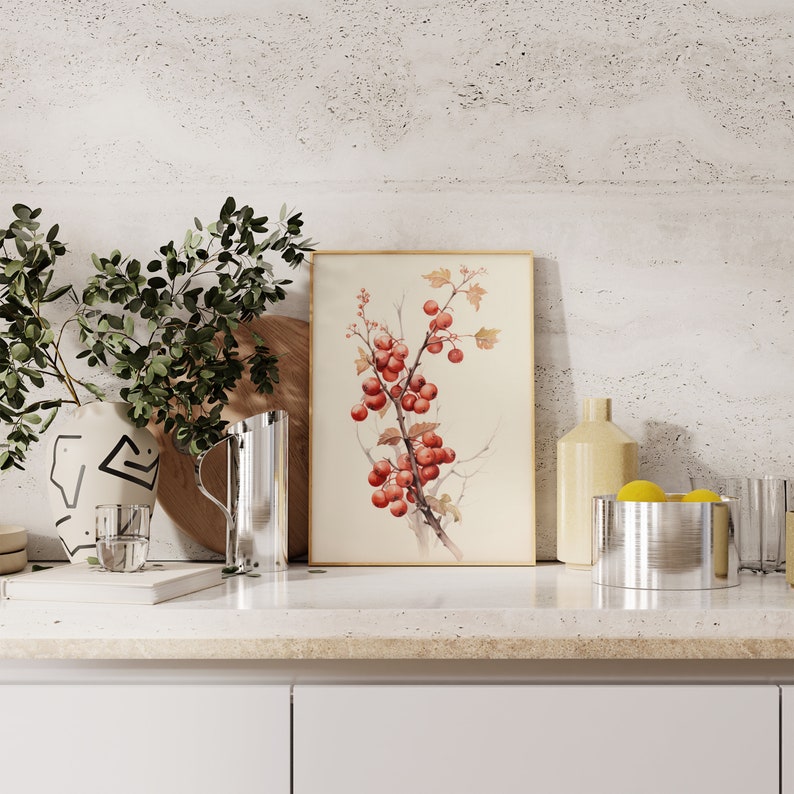 May include: A watercolor print of a red berry branch with green leaves in a light wood frame. The print is displayed on a countertop with a vase, pitcher, and other decorative items.