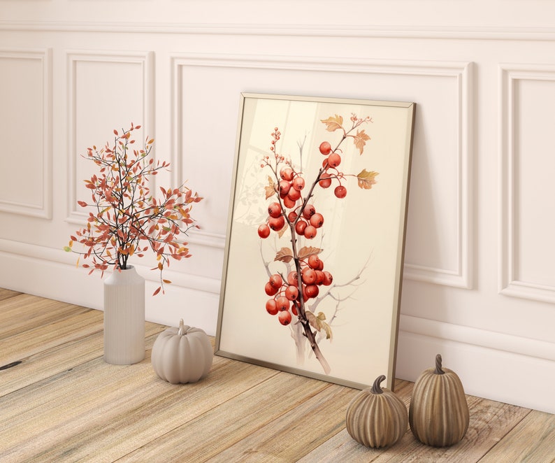 May include: A framed watercolor painting of a branch with red berries and green leaves. The painting is hanging on a white wall with a white wainscoting trim. There are two small decorative pumpkins on the floor in front of the painting.