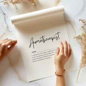 May include: A white print with the word "Aromatherapist" in black cursive lettering. The definition of the word is written below in black text: "A whisperer of scents, crafting elixirs that evoke memories and soothe the soul. Each aromatic blend is a journey to the heart's sanctuary of peace."