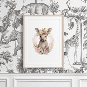 K&ouml;nnte beinhalten: Ein gerahmter Kunstdruck mit einer zentralen Illustration eines jungen K&auml;ngurus, das mit einem Blumenkranz aus zartrosa und pfirsichfarbenen Bl&uuml;ten geschm&uuml;ckt ist, vor einem schwarz-wei&szlig;en Tapetenhintergrund mit verschiedenen Dschungeltieren.