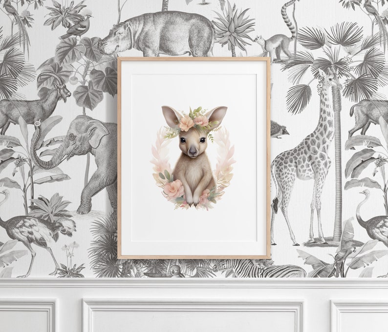 K&ouml;nnte beinhalten: Ein gerahmter Kunstdruck mit einer zentralen Illustration eines jungen K&auml;ngurus, das mit einem Blumenkranz aus zartrosa und pfirsichfarbenen Bl&uuml;ten geschm&uuml;ckt ist, vor einem schwarz-wei&szlig;en Tapetenhintergrund mit verschiedenen Dschungeltieren.