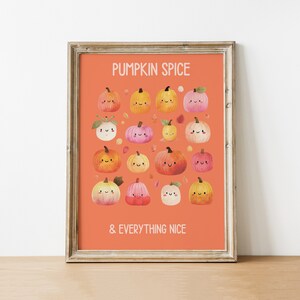 May include: A framed print with a light brown wooden frame. The print features a collection of cartoon pumpkins in various colors, with the text "PUMPKIN SPICE & EVERYTHING NICE" in white letters on an orange background.