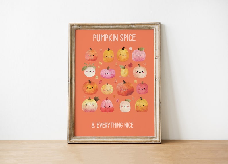 May include: A framed print with a light brown wooden frame. The print features a collection of cartoon pumpkins in various colors, with the text "PUMPKIN SPICE & EVERYTHING NICE" in white letters on an orange background.