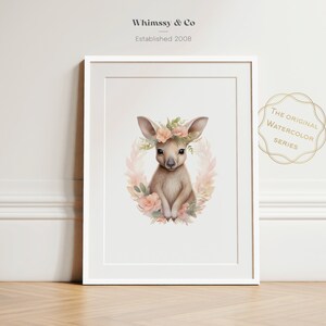 K&ouml;nnte beinhalten: Ein gerahmter Kunstdruck mit einer Aquarellillustration eines K&auml;nguru-Babys, umgeben von einem Kranz aus zartrosa Blumen und gr&uuml;nen Bl&auml;ttern. Der Text Whimssy & Co Established 2008 und The Original Watercolor Series ist zu sehen.