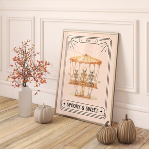 May include: A pink and white illustrated print with three skeletons riding a carousel. The print has a black frame and the text "Spooky & Sweet" at the bottom.