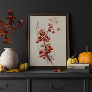 May include: A framed botanical print of a branch with red berries against a white background. The print is on a dark grey dresser with a vase of fall leaves, pumpkins, and books.