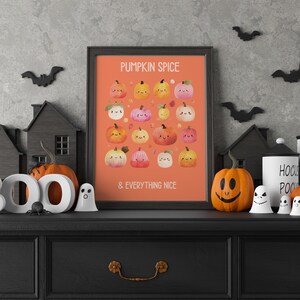 May include: A framed orange print with the text "PUMPKIN SPICE & EVERYTHING NICE" and illustrations of smiling pumpkins. The print is displayed on a black dresser with Halloween decorations, including pumpkins, ghosts, and bats.