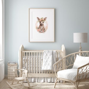 K&ouml;nnte beinhalten: Ein gerahmter Kunstdruck mit einer Aquarellillustration eines jungen K&auml;ngurus, das in einem Kranz aus zartfarbenen Blumen sitzt. Das K&auml;nguru hat gro&szlig;e Ohren und ist von rosa und pfirsichfarbenen Bl&uuml;ten sowie gr&uuml;nem Blattwerk umgeben.
