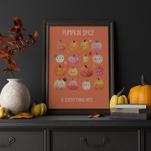 May include: A framed print with the text "PUMPKIN SPICE & EVERYTHING NICE" and illustrations of smiling pumpkins in various colors. The print is displayed on a black dresser, alongside pumpkins, a vase, and fall foliage.