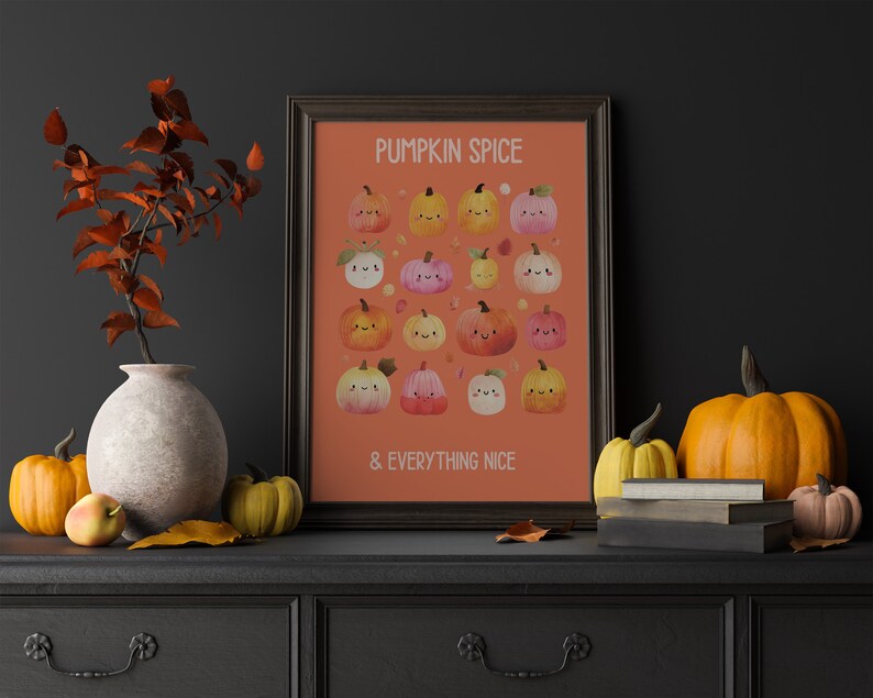 May include: A framed print with the text "PUMPKIN SPICE & EVERYTHING NICE" and illustrations of smiling pumpkins in various colors. The print is displayed on a black dresser, alongside pumpkins, a vase, and fall foliage.