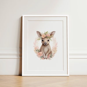 K&ouml;nnte beinhalten: Ein gerahmter Kunstdruck mit einer Aquarellillustration eines jungen K&auml;ngurus, das von einem Kranz aus zartrosa Bl&uuml;ten und gr&uuml;nen Bl&auml;ttern umgeben ist. Das K&auml;nguru hat gro&szlig;e Ohren und ist in hellbraunen und cremefarbenen T&ouml;nen gehalten.
