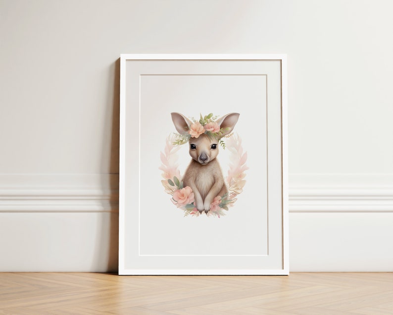 K&ouml;nnte beinhalten: Ein gerahmter Kunstdruck mit einer Aquarellillustration eines jungen K&auml;ngurus, das von einem Kranz aus zartrosa Bl&uuml;ten und gr&uuml;nen Bl&auml;ttern umgeben ist. Das K&auml;nguru hat gro&szlig;e Ohren und ist in hellbraunen und cremefarbenen T&ouml;nen gehalten.