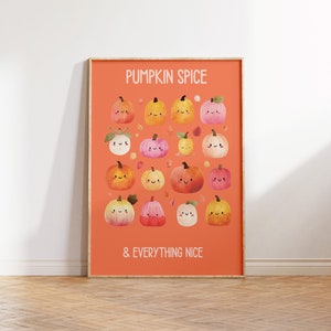May include: A framed orange print featuring a collection of cartoon pumpkins in various colors, each with a smiling face. The text "PUMPKIN SPICE & EVERYTHING NICE" is displayed in white. The print is displayed on a wooden floor.