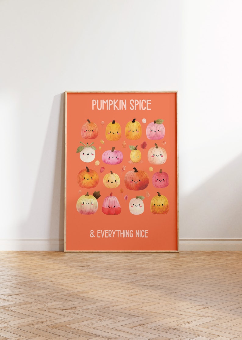 May include: A framed orange print featuring a collection of cartoon pumpkins in various colors, each with a smiling face. The text "PUMPKIN SPICE & EVERYTHING NICE" is displayed in white. The print is displayed on a wooden floor.