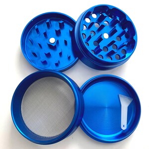 Puede incluir: Un molinillo de hierbas de metal azul de cuatro piezas desmontado en sus componentes individuales. El conjunto incluye dos tapas de molienda con dientes afilados, una secci&oacute;n central con una malla met&aacute;lica fina, una bandeja de recolecci&oacute;n y una peque&ntilde;a esp&aacute;tula de pl&aacute;stico blanco.