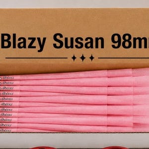 Może przedstawiać: Kartonowe pudełko z brązową pokrywką z czarnym napisem Blazy Susan 98mm i trzema ikonami diamentów. Wewnątrz pudełka znajduje się wiele różowych papierowych stożków, z których każdy ma nadrukowaną nazwę marki Blazy Susan w układzie poziomym.