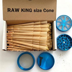 May include: A cardboard box labelled RAW KING size Cone filled with numerous light brown paper cones. Beside the box are several blue metal circular grinder components, including a lid, a base with teeth, a mesh screen, and a small black scraper.