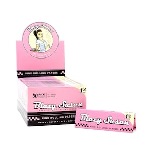 May include: A display box and individual packs of pink Blazy Susan rolling papers. The packaging is pink with black and white checkered detailing. The brand logo features a woman with a tray. Each pack contains 50 leaves.