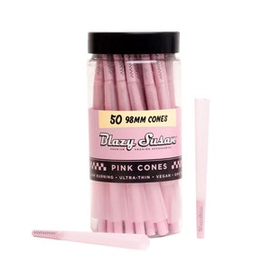 May include: A clear plastic container with a black lid holds 50 pink 98mm cones. The label reads "Blazy Susan Pink Cones" with text indicating slow burning, ultra-thin, vegan, and GMO-free. Two pink cones are outside the container.