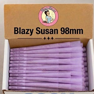 May include: A cardboard box containing a stack of light purple pre-rolled cones. The box lid features a circular logo with a woman and the text Blazy Susan 98mm. Each individual cone is printed with the brand name Blazy Susan in a small font.