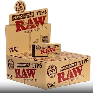 Puede incluir: Una caja de puntas RAW anchas perforadas para enrollar cigarrillos. La caja es marrón con el logotipo RAW en rojo y blanco. El texto "Authentic Soft Tips" está impreso en la caja. La caja está sentada en una mesa con otras cajas de puntas RAW.
