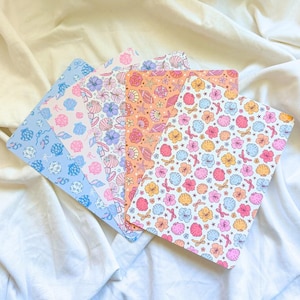 May include: A set of five rectangular cards arranged in a fan shape, each featuring a repeating pattern of seashells, starfish, and small flowers in various color palettes including blue, pink, orange, and white with small ribbon accents.