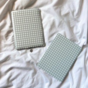 May include: Two green and white gingham patterned cases for a tablet and a phone. The tablet case has a silver heart charm attached.