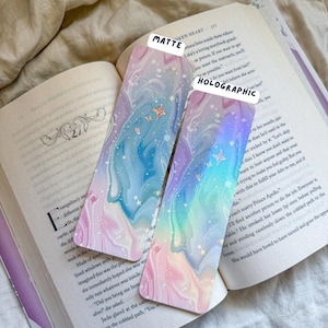May include: Two decorative bookmarks with a dreamy, marbled design in pastel colors. One is matte, the other holographic, with text labels. The bookmarks feature a swirling pattern of blues, pinks, and purples, with small star and butterfly accents.