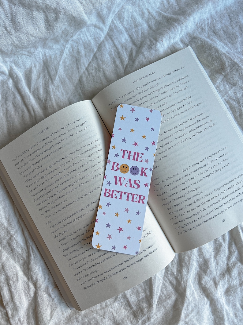 May include: A white bookmark with a pink, purple, and yellow star pattern. The bookmark has the text "The Book Was Better" with a smiley face.