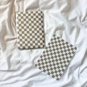 May include: Two clear phone cases with a black and white checkered pattern. The cases are lying on a white bed sheet.
